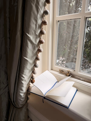 Open book on a windowsill with a decorative curtain and window view.
