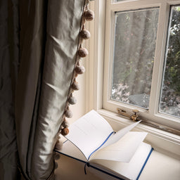 Open book on a windowsill with a decorative curtain and window view.
